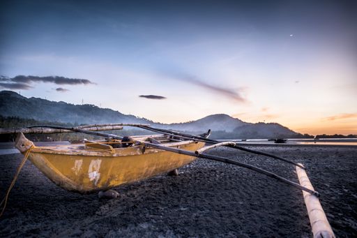 A closeup shot of a boat on the shore with mountains and a beautiful sky in the background