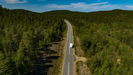 Aerial view of a camper driving in middle of forest, and tunturi mountains, in Inari, Lapland, Finland