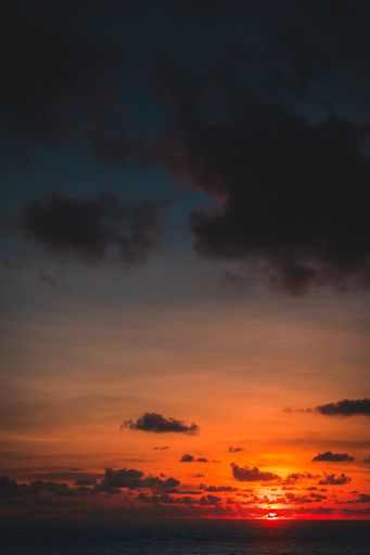 A vertical shot of the ocean with the sun going down behind the clouds in the background in Bali