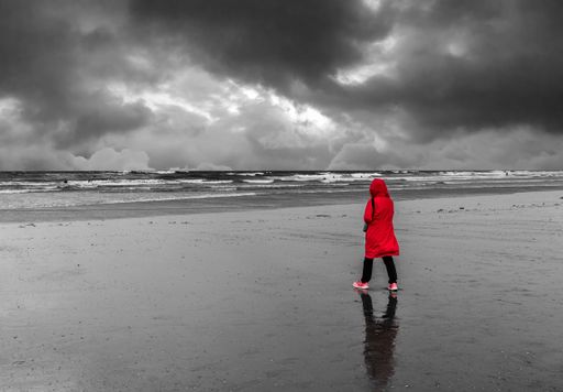 A selective color shot of a female in red coat at the beach in black and white