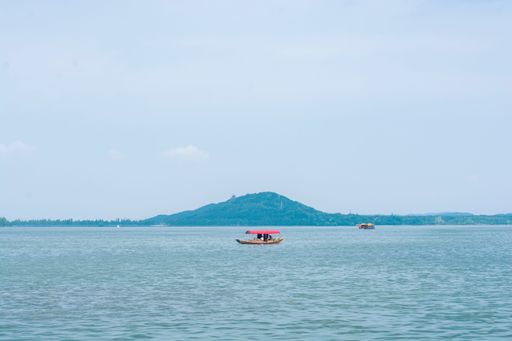 A boat floating in the middle of a beautiful sea with a mountain in the background under a clear sky