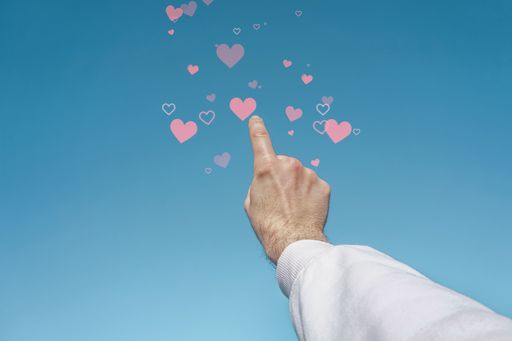 A low angle shot of a man's hand pointing out 3D rendered pink heart icons
