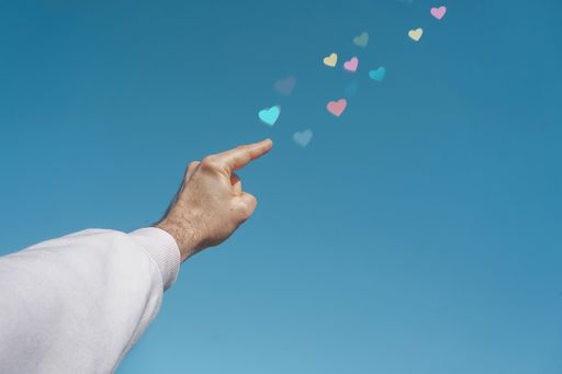 A low angle shot of a man's hand pointing out 3D rendered colorful heart icons
