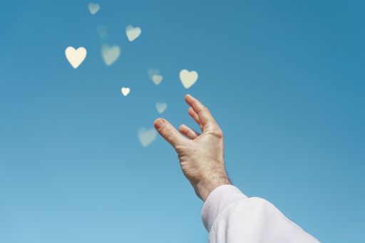 A low angle shot of a man's hand presenting a out 3D rendered yellow heart icons above his palm