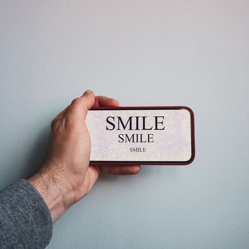 A man's hand holding a phone with rendered screen on which there is written smile for three times
