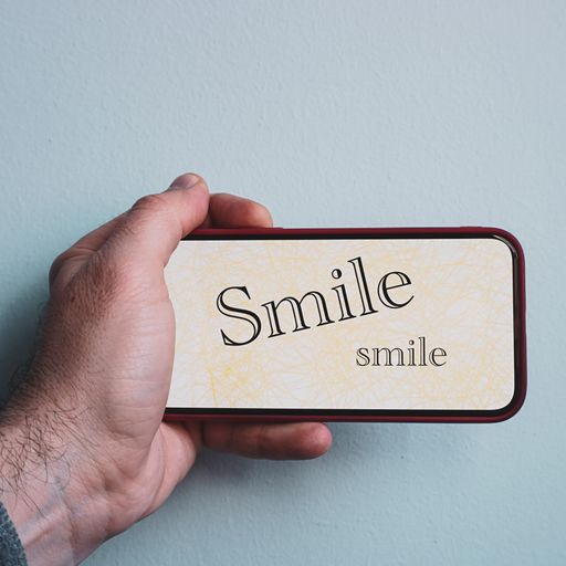 A man's hand holding a phone with rendered screen on which there is written smile