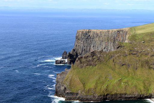 A mesmerizing view of the rocky cliff of Moher in county Clare in Ireland, covered by grass, and a breathtaking view of a seascape on a sunny day