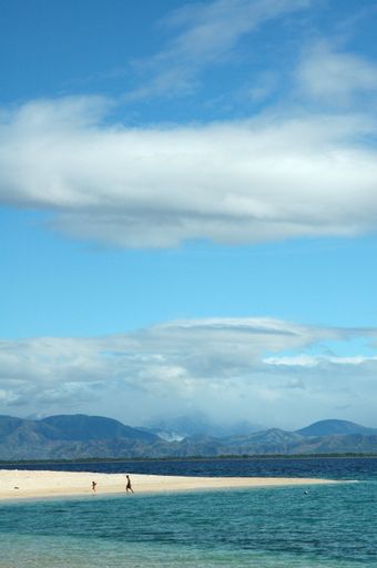 A vertical shot of a beach near the beautiful sea surrounded by high mountains under the cloudy sky