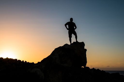 A person standing on a rock on the beach at sunset