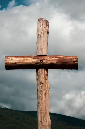 A vertical shot of a wooden cross under a cloudy sky