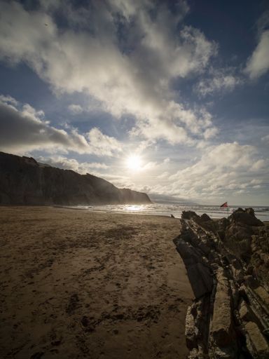 A vertical shot of rocks in a beach surrounded by the sea under the sunlight during the sunrise