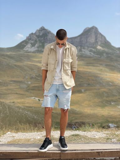 A vertical shot of a stylish young man standing against a beautiful mountains landscape