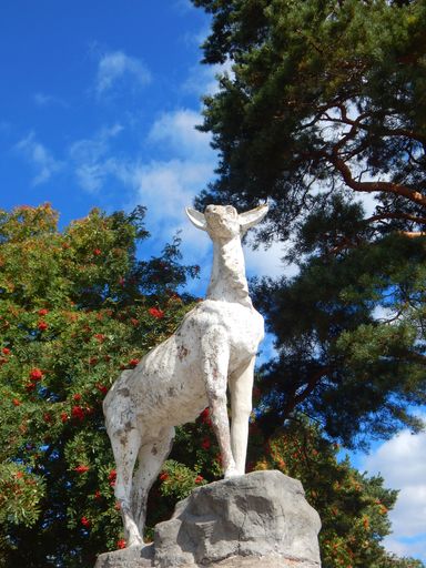 A low angle vertical shot of a doe statue in the park on the background of green trees