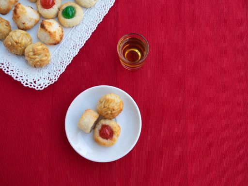 A flat lay of a plate and tray of tasty panellets with a glass of drink on a red table