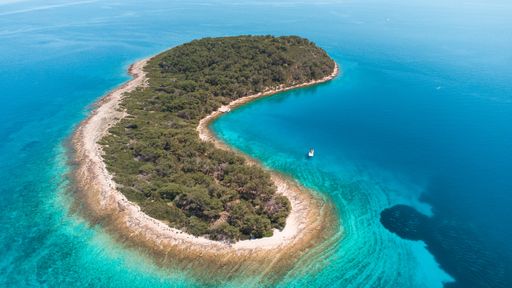 An aerial shot of an island with a boat on the blue water on a sunny day