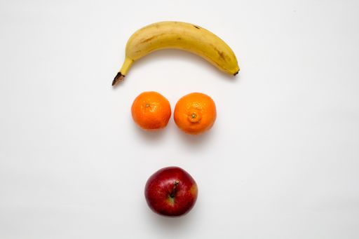 A flat lay of a banana, oranges and an apple on white surface