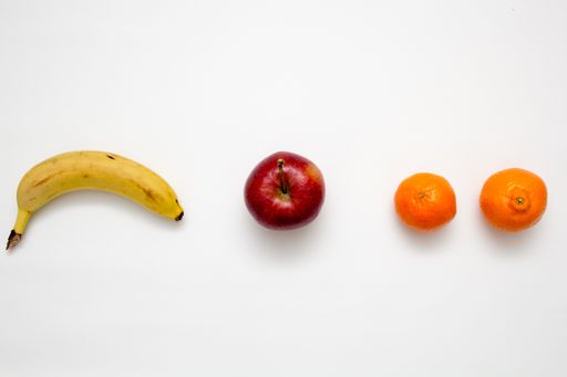A flat lay of a banana, oranges and an apple on white surface