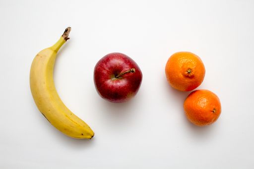 A closeup shot of fruit including banana and apple and mandarins on a white background