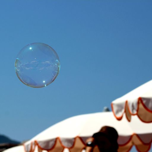 A closeup shot of a soap bubble floating in the air against a blue sky