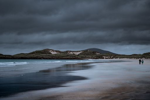 The couple walking along a sandy coastline in Donegal on a cloudy day