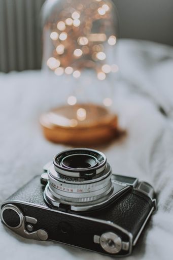 A vertical selective focus shot of a vintage camera and a nice lantern on a white surface
