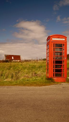 A vertical shot of a red telephone booth by the road. Edinburgh, Scotland.