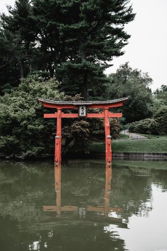 A Japanese torii reflected in waters with trees in the background under a cloudy sky