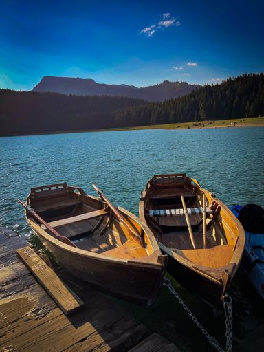 A vertical closeup shot of two canoe wooden boats on a pier with a lake surrounded by trees in the background