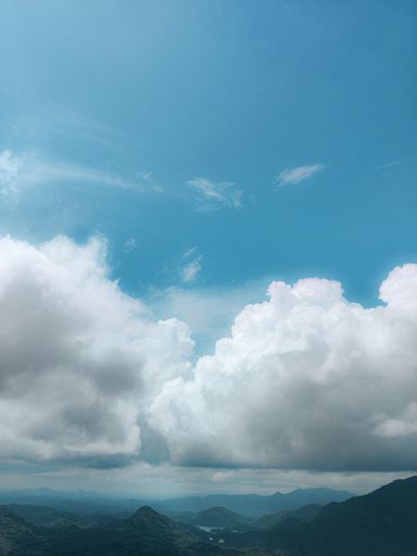 A vertical aerial shot of the blue sky with heavy white clouds over the mountains