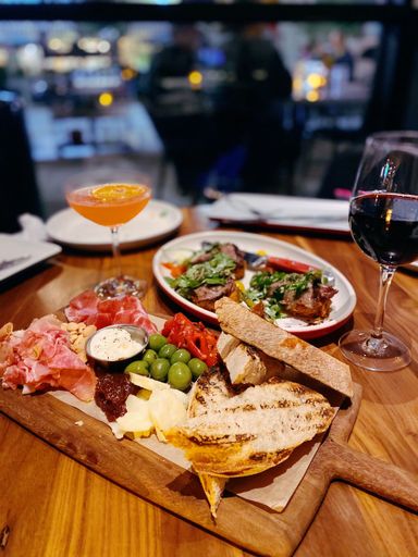 A vertical closeup shot of an Italian dinner with a meat and cheese platter and drinks