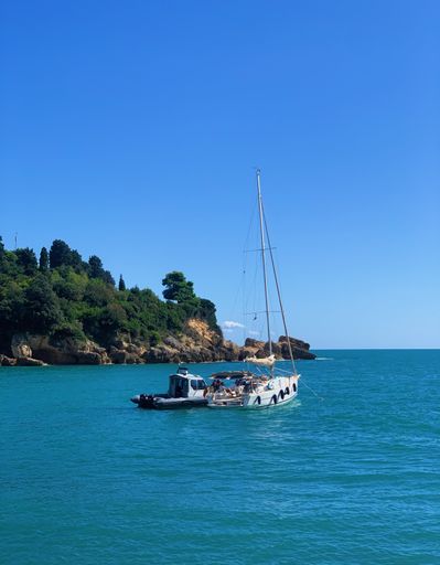 A vertical closeup shot of a white boat on clear ocean water with a hill in the background
