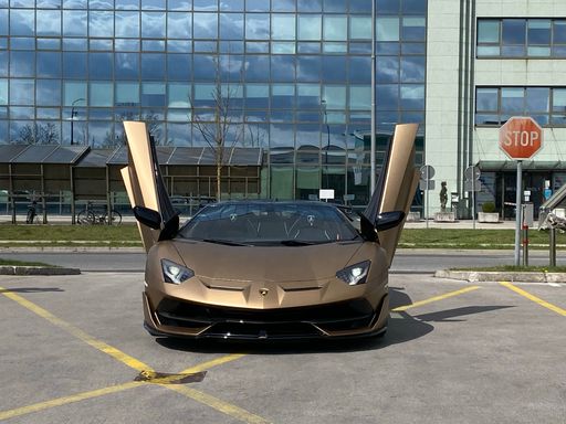 A Lamborghini Aventador SVJ brown color in front of a modern building