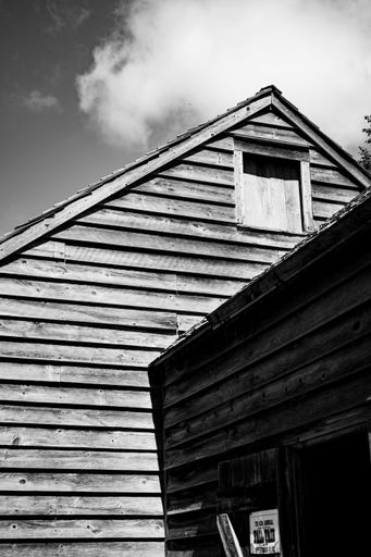 A vertical grayscale shot of wooden village house under cloudy sky in Quebec, Canada
