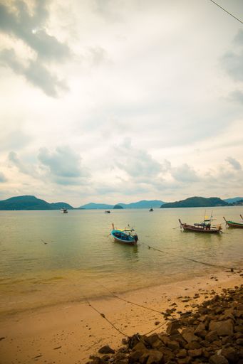 A vertical shot of small boats in the sea next to the shore on a cloudy day