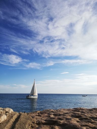 A vertical shot of a ship sailing near the rocky coast