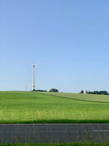 A vertical shot of a modern windmill on a green field against a blue sky
