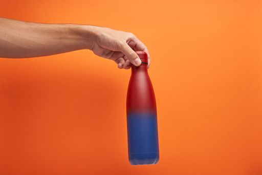 A hand holding a colorful thermal bottle on an orange background