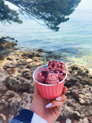 A vertical shot of a hand holding pink icecream at he shore