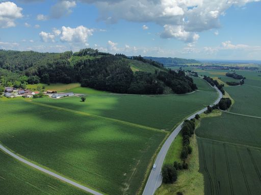 A Drone shot over forested mountains and a village surrounded by green fields