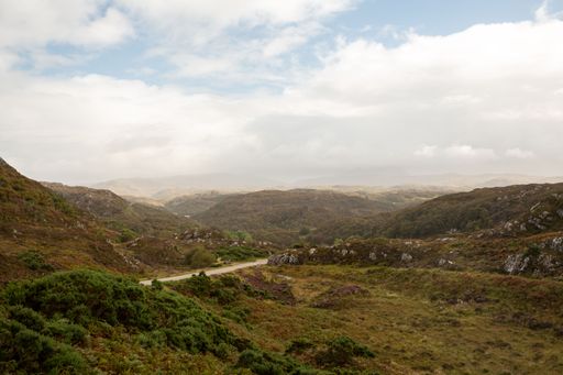 A beautiful view over a narrow road surrounded the mountains and hills on a gloomy day
