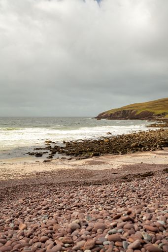 A vertical shot of a rocky beach with the foamy sea and the horizon in the background on a gloomy day