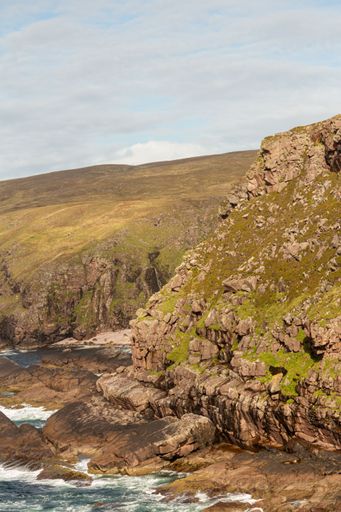 A vertical shot of a cliff and the foamy sea under the blue sky during the daytime