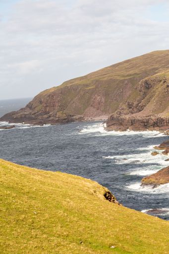 A vertical shot of a cliff and the foamy sea under the blue sky during the daytime