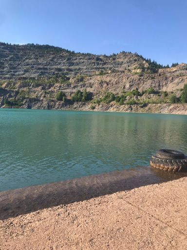A beautiful view of sand beach by a lake under green mountains around under blue sky