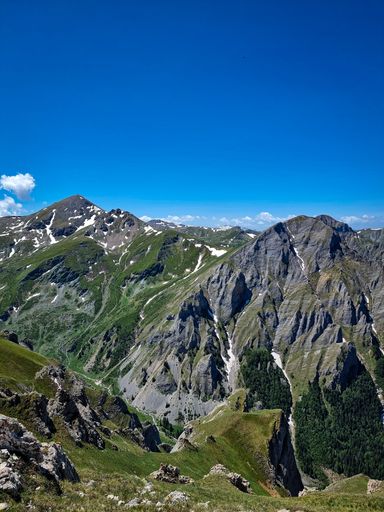 A gorgeous landscape with tall mountains and green fields under a bright blue sky on a sunny day