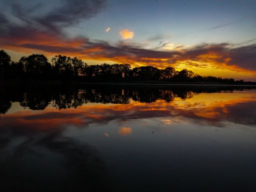 A gorgeous sunset over a reflective lake with silhouettes of trees under orange and blue clouds