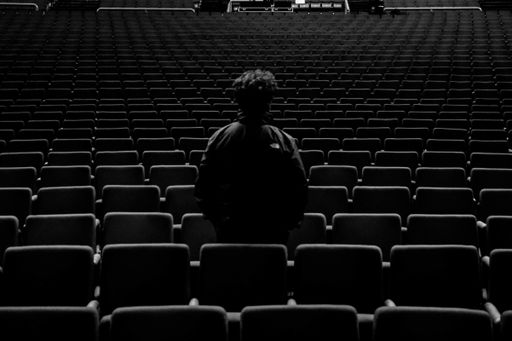A greyscale shot of a person standing in an empty theatre  - concept: loneliness