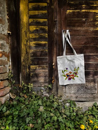 A vertical shot of a embroidered tote bag hanging from a wooden door with green leaves around