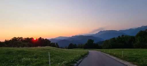 A green field with a road at sunset against a cloudy sky with mountains in the background