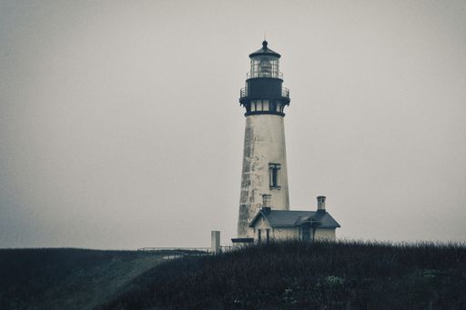 A gray scale shot of a lighthouse and a house on a hill covered with grass under the clear sky
